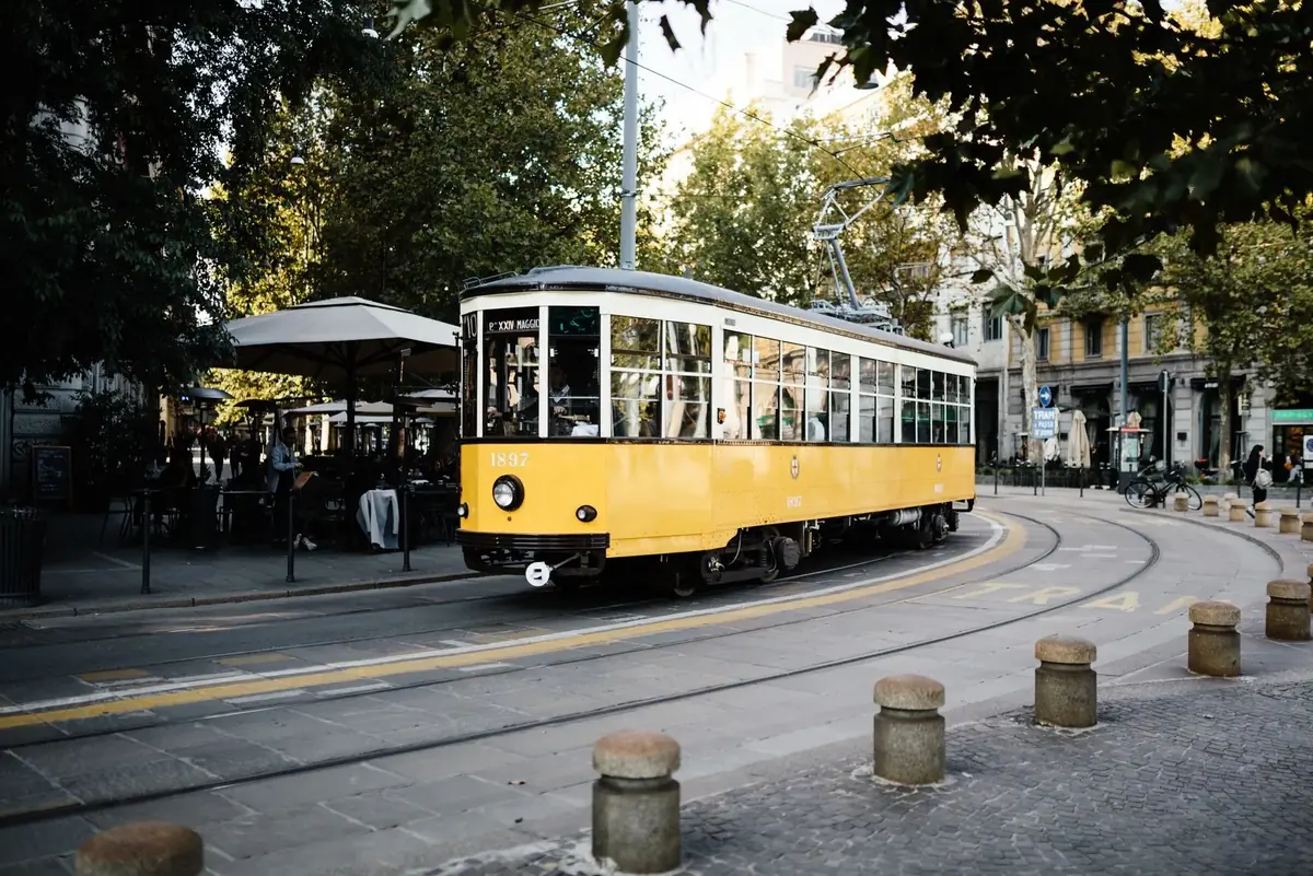 A yellow Milan tram on a tree-lined street
