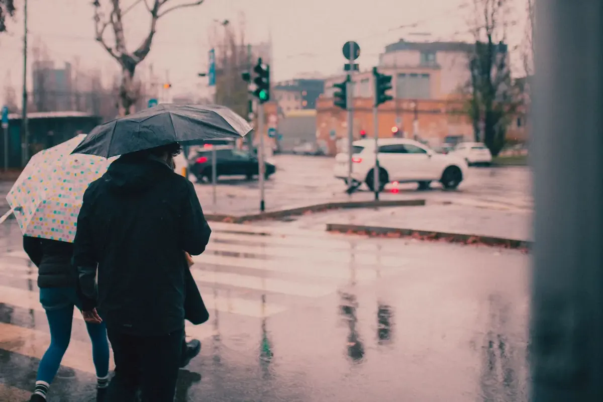 Pedestrians with umbrellas crossing a wet Milan street